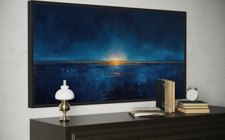 Abstract navy blue and gold ocean painting in a black frame above a dark wood dresser.