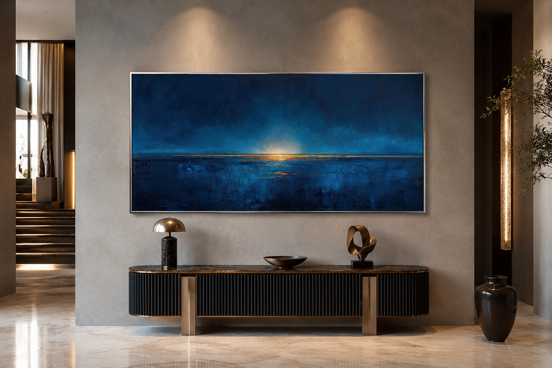 Abstract navy blue and gold ocean horizon painting in a silver frame above a black console table.