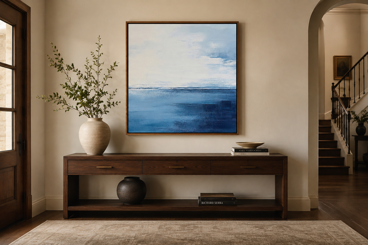 Abstract square framed canvas art with navy blue, grey, and silver ocean horizon over a console.