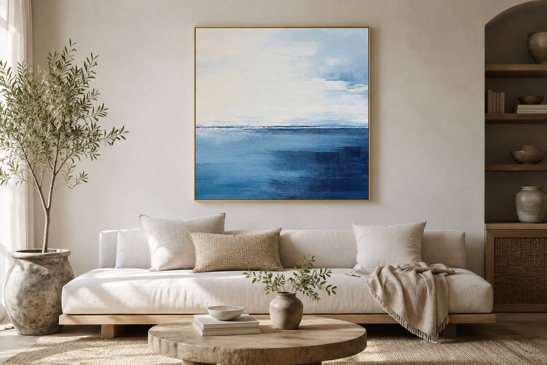 Square framed abstract ocean canvas art with navy blue, grey, and silver tones above a white sofa.
