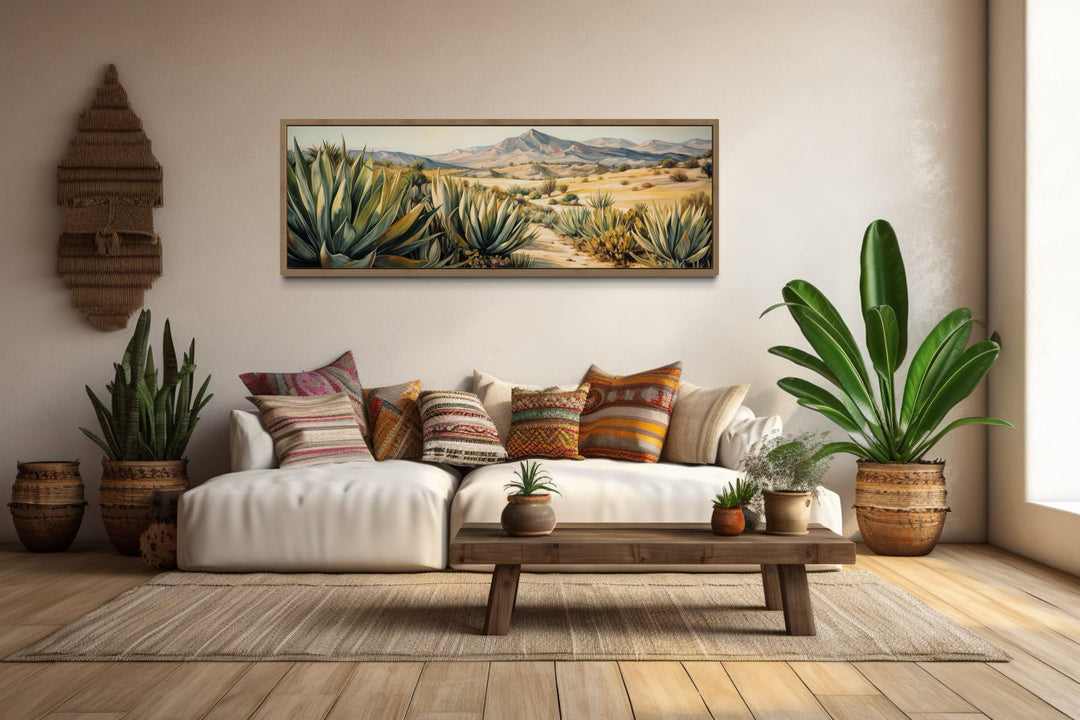 Horizontal framed canvas wall art of agave plants in a desert landscape above a white sofa.