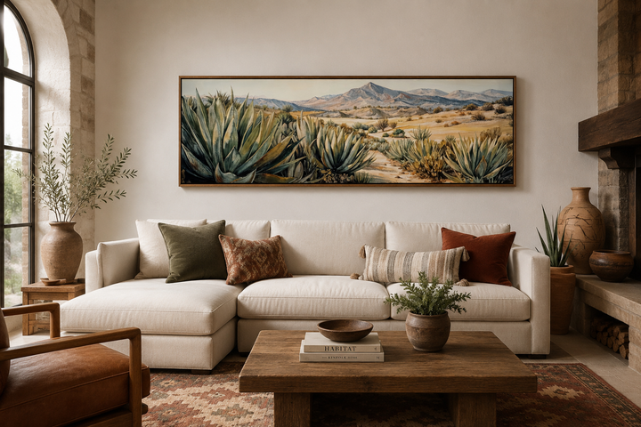 Horizontal framed canvas wall art of agave plants in a desert landscape above a white sofa.