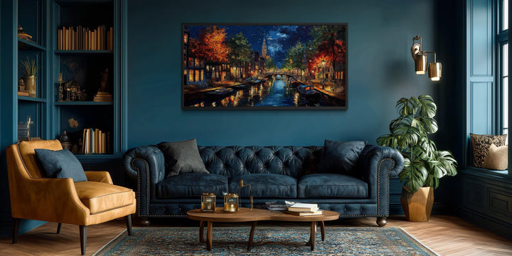 A large horizontal canvas of an Amsterdam canal at night hangs in a moody, dark blue living room.