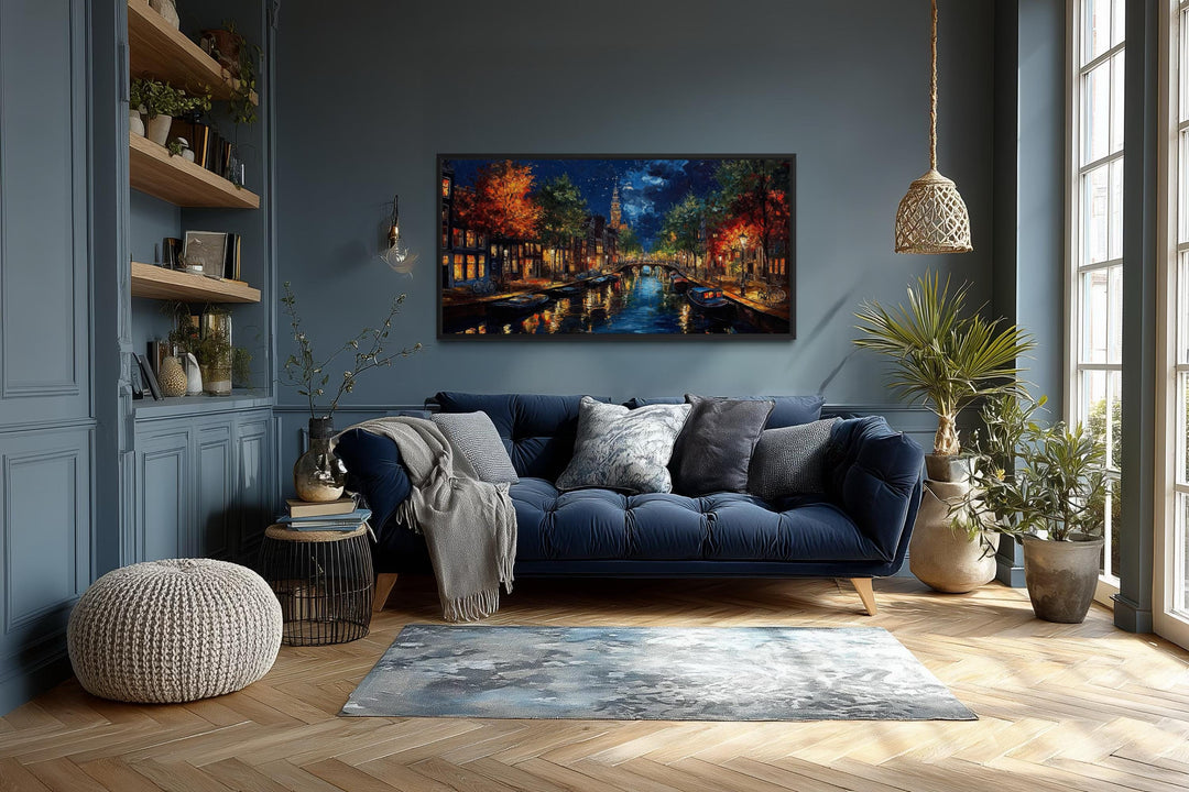 Large horizontal canvas wall art of an Amsterdam canal at night above a blue sofa in a living room.