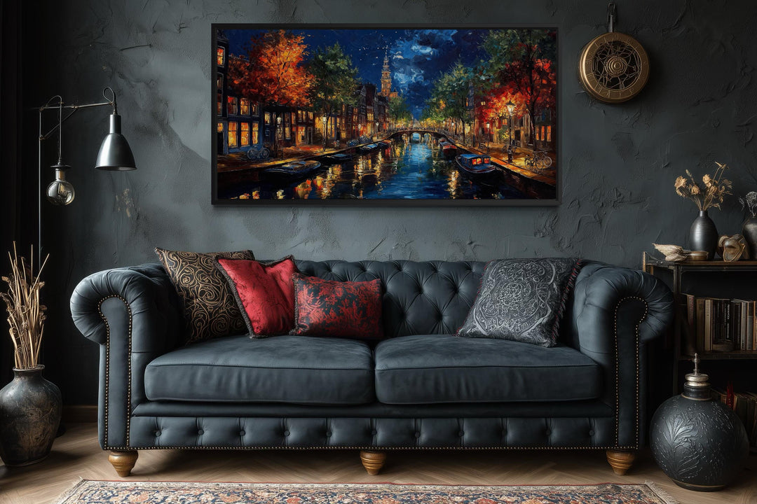 Large horizontal canvas wall art of an Amsterdam canal at night above a dark sofa in a moody room.