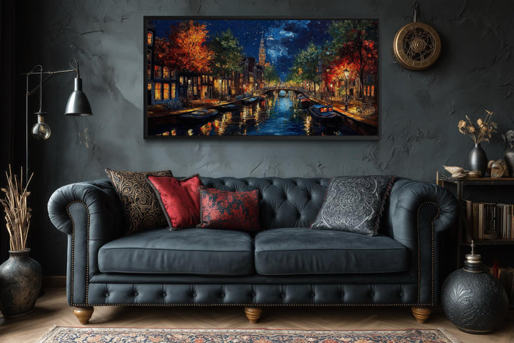 Large horizontal canvas wall art of an Amsterdam canal at night above a dark sofa in a moody room.