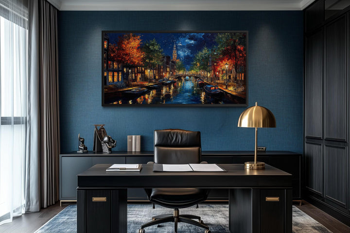 Large horizontal canvas wall art of an Amsterdam canal at night hanging in a dark, modern office.