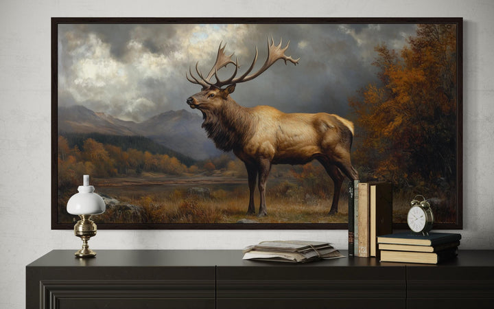 Antique elk canvas wall art in a dark frame above a dresser with a lamp, books, and clock.