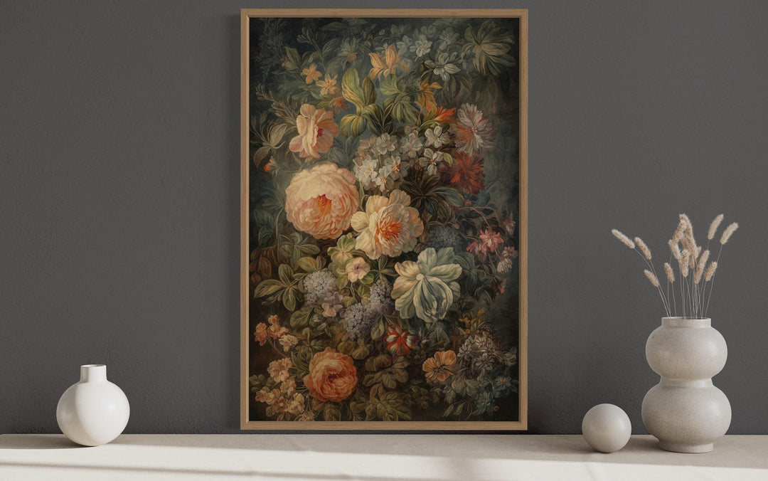 a large floral painting hanging on a wall, with a vase of flowers placed to the right of the painting.