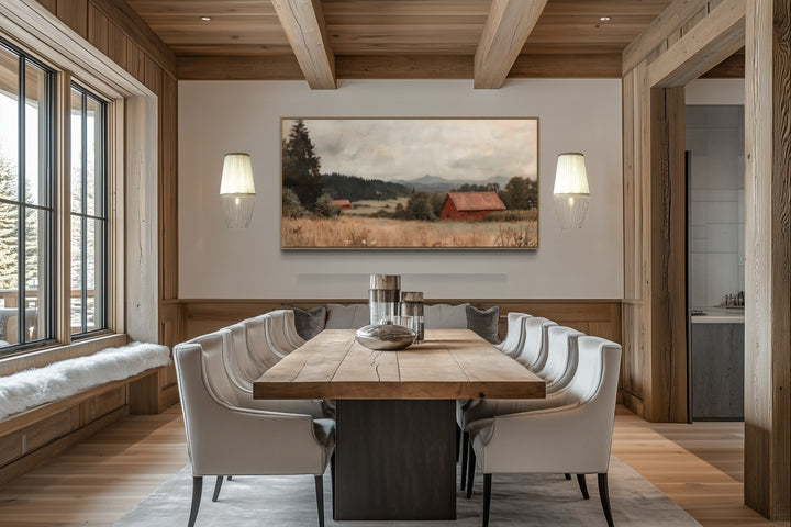 Antique red barn canvas print in a rustic dining room with a large wooden table and grey chairs.