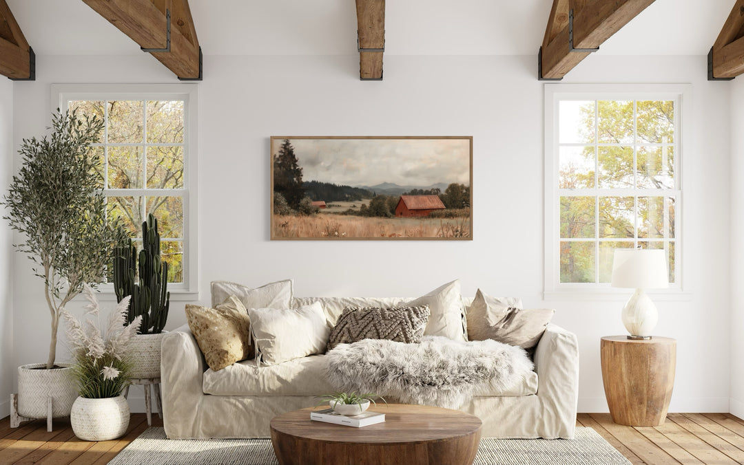 Antique red barn canvas print in a wooden frame hanging above a neutral sofa in a farmhouse room.