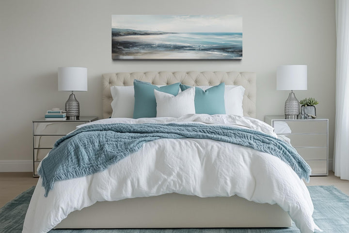 Aqua blue ocean beach coastal wall art in a long horizontal frame hanging over a bed.