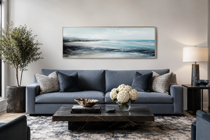 Framed horizontal canvas wall art of an aqua blue ocean seascape hanging above a blue sofa.