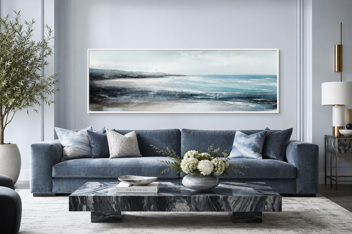 Panoramic aqua blue ocean beach framed canvas wall art displayed over a blue sofa in a living room.