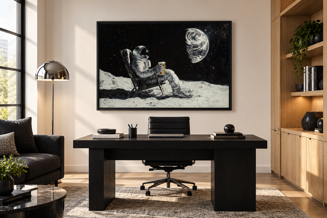 Framed canvas wall art of an astronaut drinking beer on the moon, hung above a black office desk.