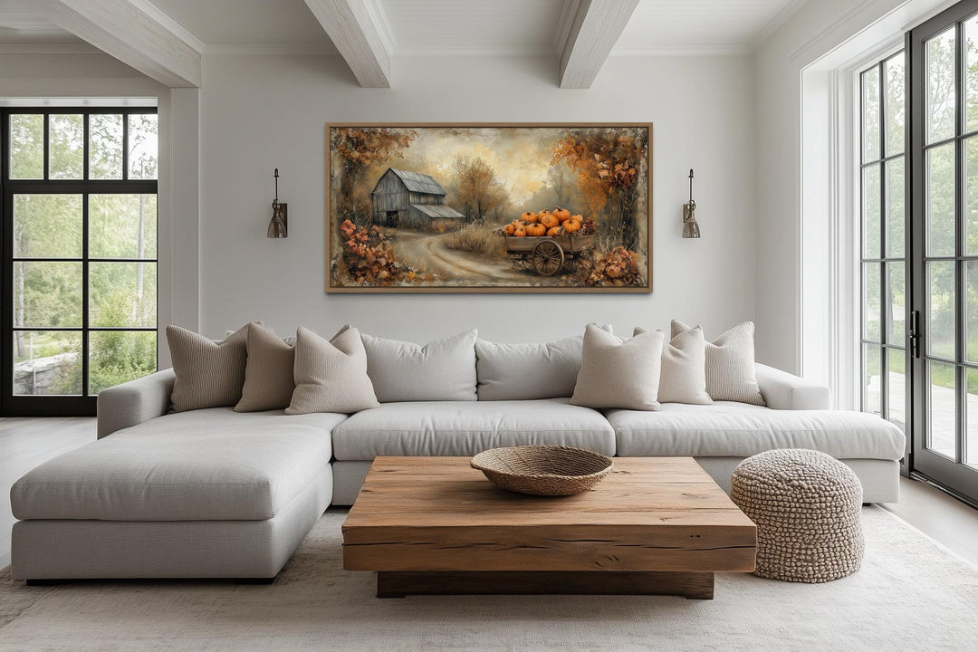 Autumn Barn and Pumpkin Cart canvas wall art hanging above a light gray sofa in a living room.