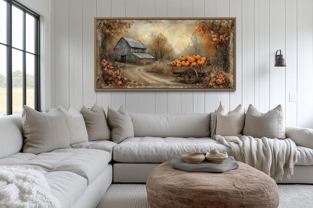 Autumn barn and pumpkin cart farmhouse canvas wall art above a neutral sectional sofa.