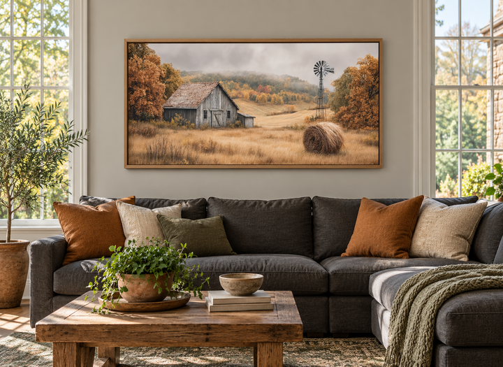 Rustic barn, hay bale, and windmill in a fall landscape canvas wall art above a dark gray sofa.