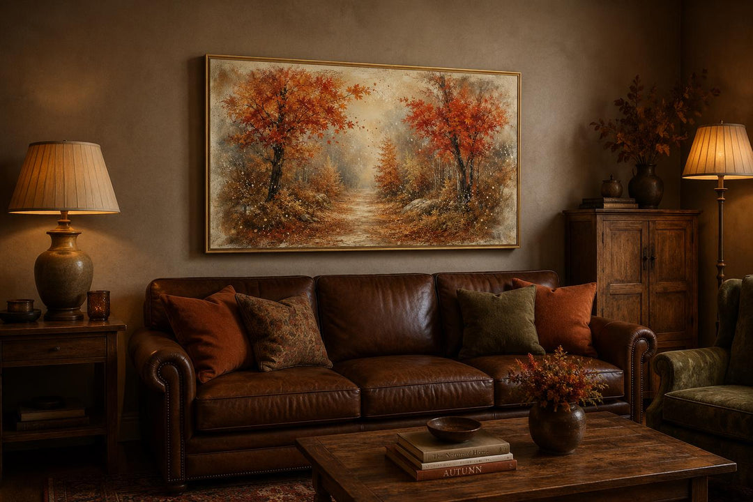 Autumn forest wall art with orange and rust trees on a canvas above a brown leather sofa.