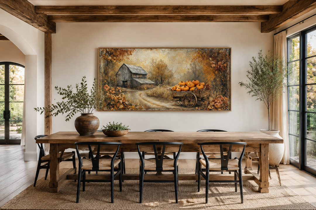 Autumn barn and pumpkin cart canvas wall art above a wooden dining table in a farmhouse room.