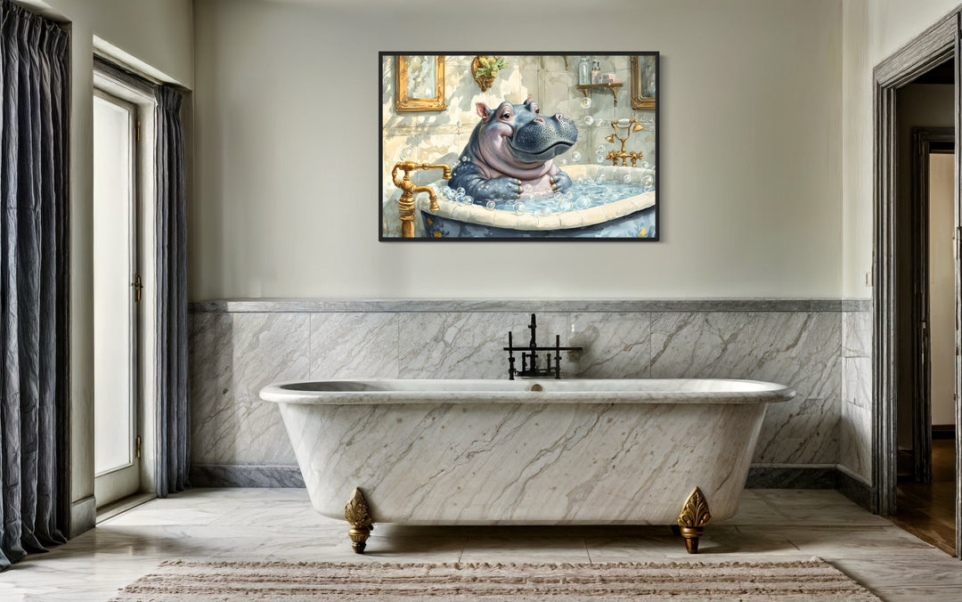 Framed canvas wall art of a baby hippo in a bathtub hanging above a marble clawfoot tub.
