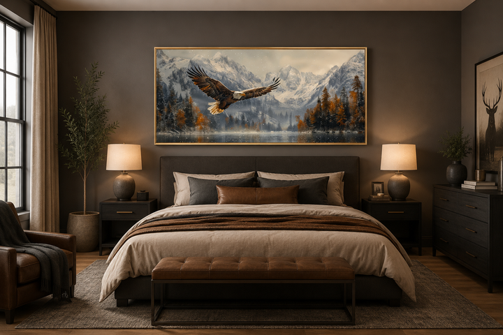 Framed canvas art of a bald eagle flying over a snowy mountain lake above a bed in a modern bedroom.