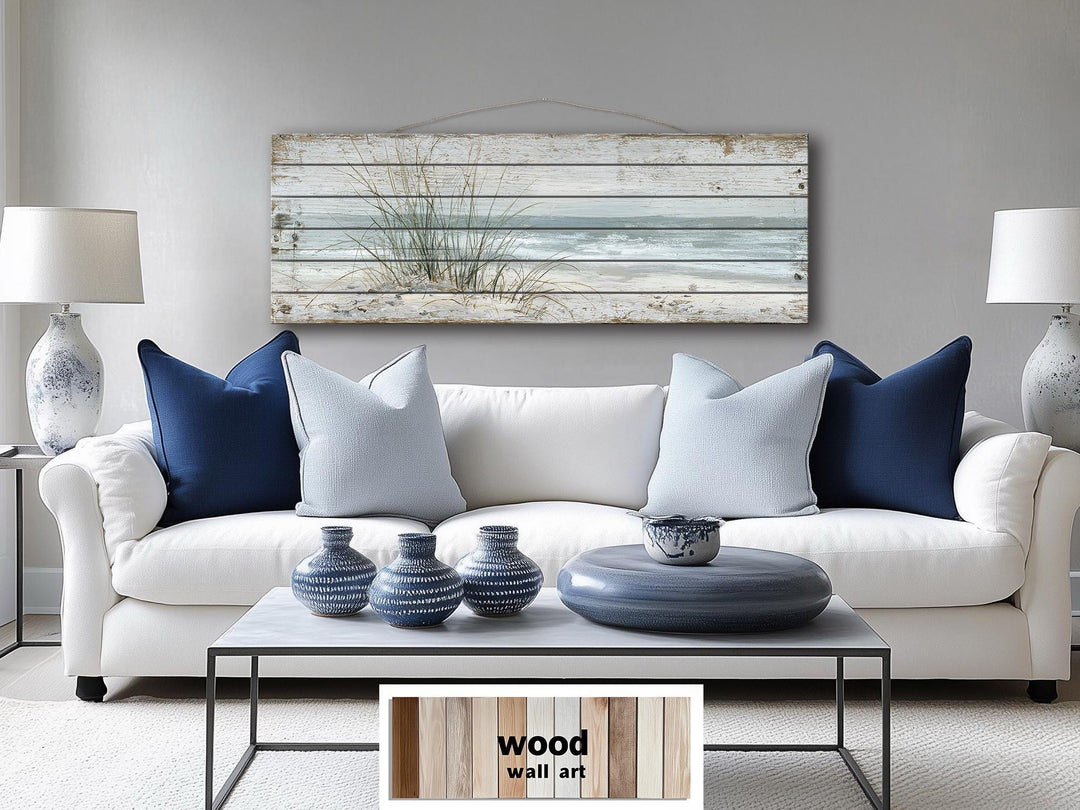 Long narrow wood wall art featuring beach sand dunes and sea grass hanging above a white sofa.