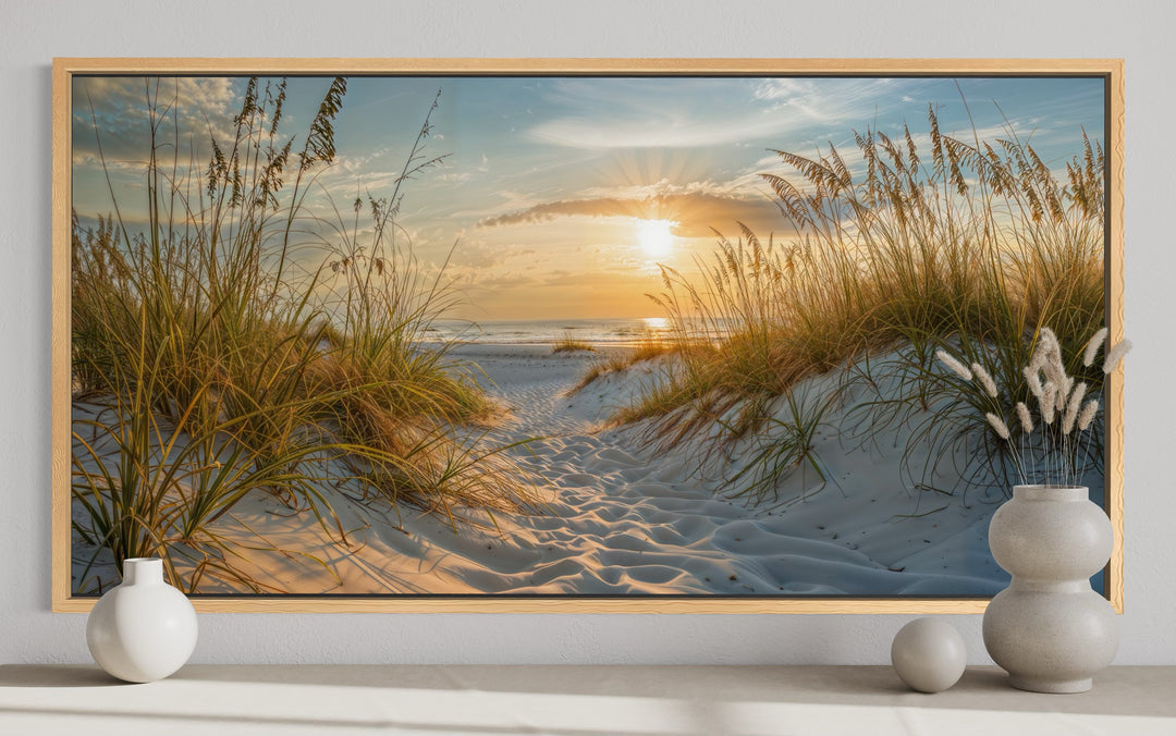 Framed canvas wall art of a beach sunset with sand dunes and sea grass in a coastal living room.