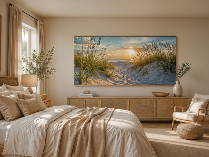 Framed beach sunset wall art featuring sand dunes and ocean view above a wooden dresser in a bedroom.