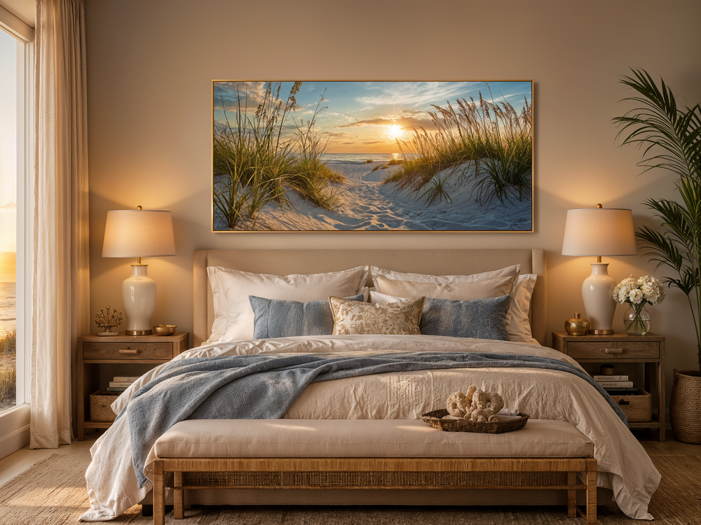 Framed beach sunset wall art featuring sand dunes and ocean above a bed in a coastal bedroom.
