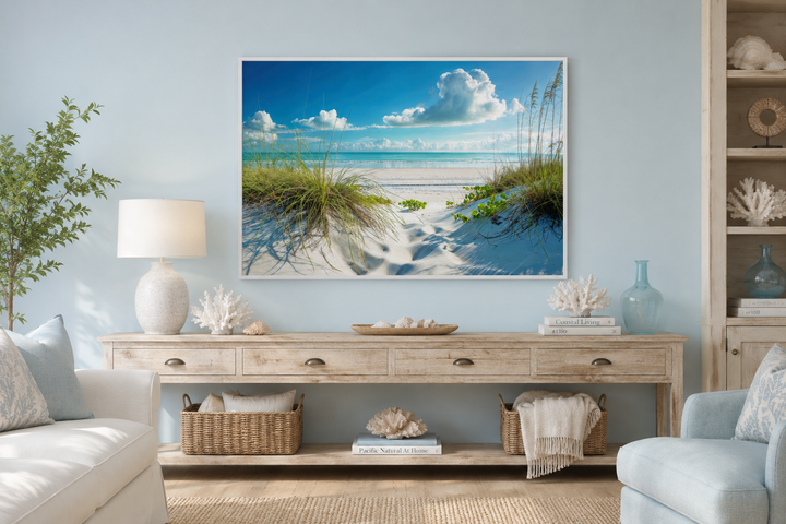 Framed beach wall art of sand dunes and grass above a wooden console table in a coastal living room.