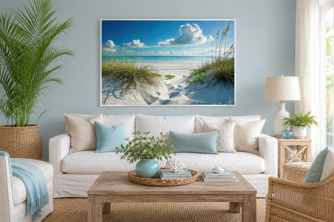 Framed coastal canvas wall art of sand dunes and grass on a beach above a white sofa.