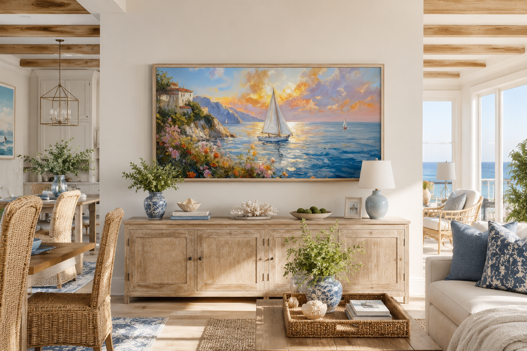 Framed coastal canvas print of a sunset seascape with sailboats above a wooden sideboard.