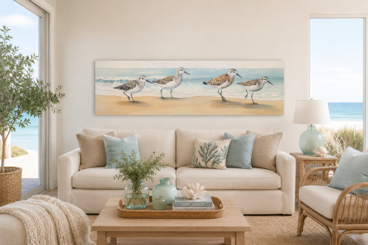 Horizontal framed canvas wall art of four sandpipers walking on a sandy beach by the ocean.