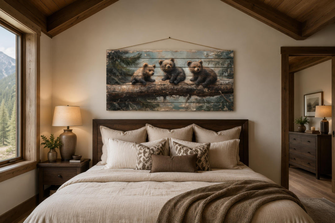 Rustic wood panel print of three bear cubs on a log, hanging above a bed in a cabin-style bedroom.