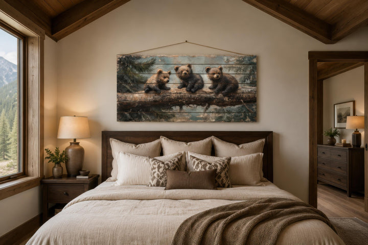 Rustic wood panel print of three bear cubs on a log, hanging above a bed in a cabin-style bedroom.