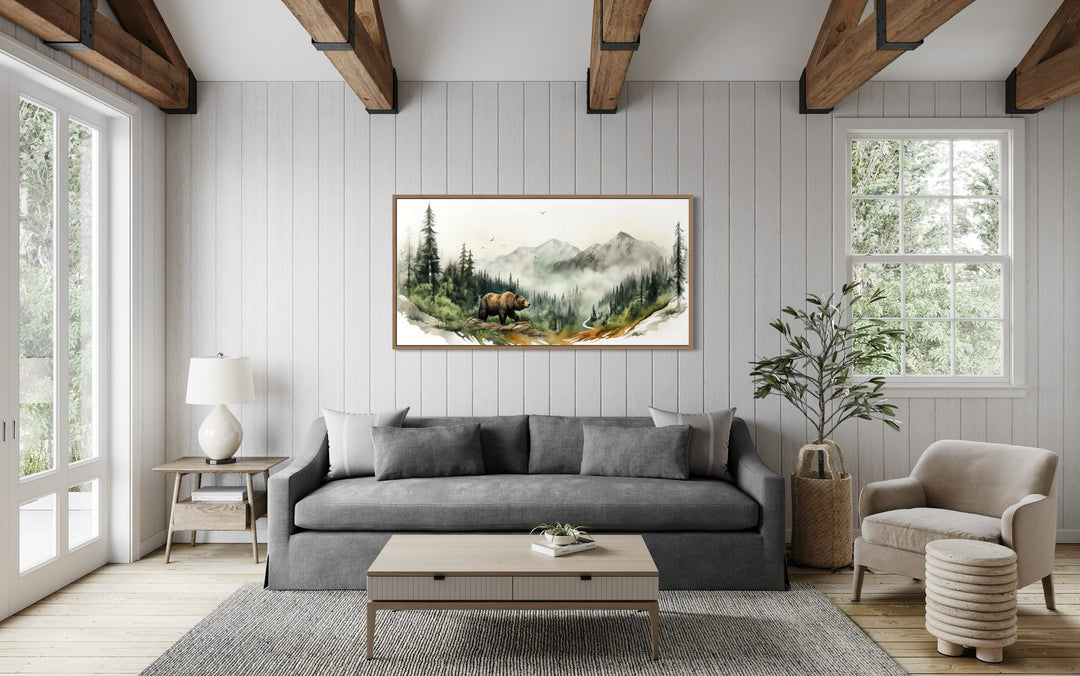 Bear in the forest mountain landscape wall art in a rustic living room above a grey sofa.