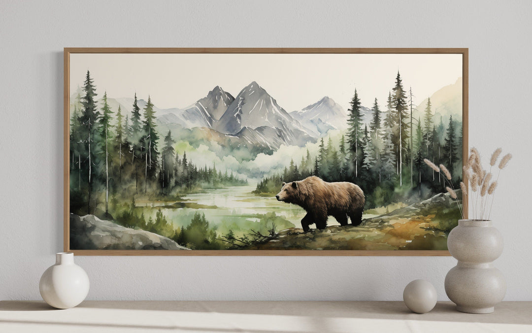 Framed watercolor painting of a bear in a mountain forest, displayed above a minimalist shelf.