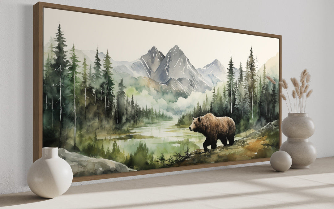 Large framed watercolor painting of a bear in a mountain forest landscape on a neutral wall.