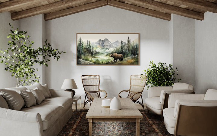 Large bear watercolor painting on canvas, framed and hung in a rustic living room above two chairs.