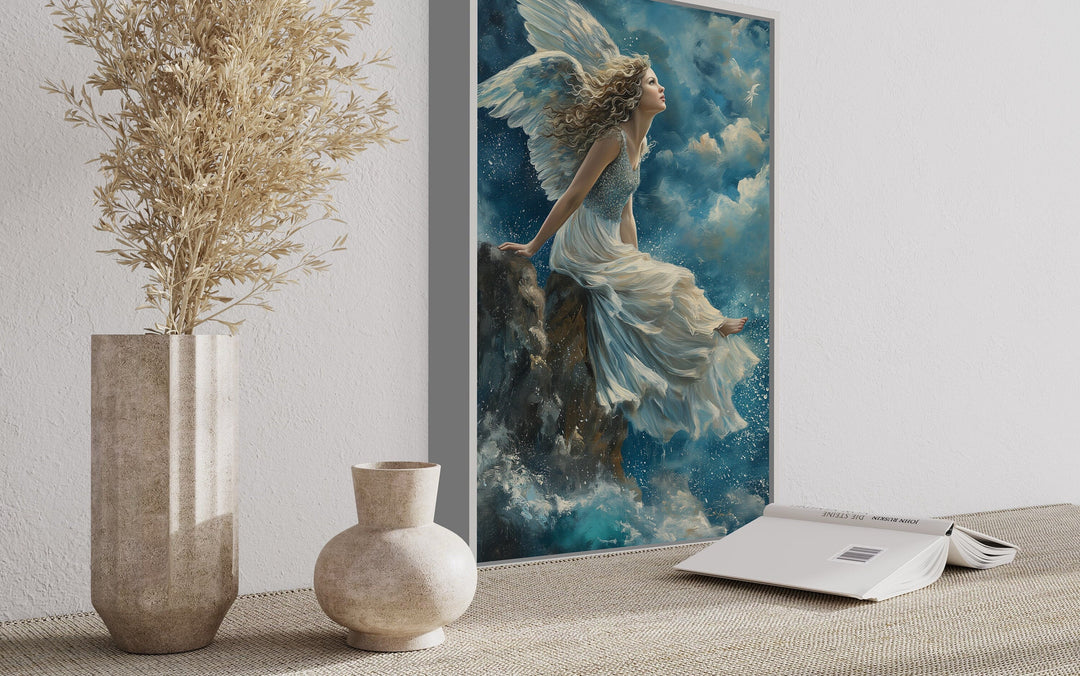 Framed Christian wall art of an angel sitting on a mountain among clouds in a serene room setting.