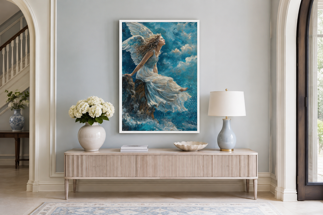 Framed wall art of an angel in a white dress sitting on a mountain peak among blue clouds.