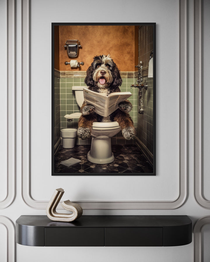 Framed canvas wall art of a Bernedoodle dog sitting on a toilet reading a newspaper in a bathroom.