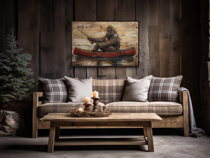 Bigfoot in a canoe rustic framed canvas wall art hanging above a sofa in a cabin-style room.