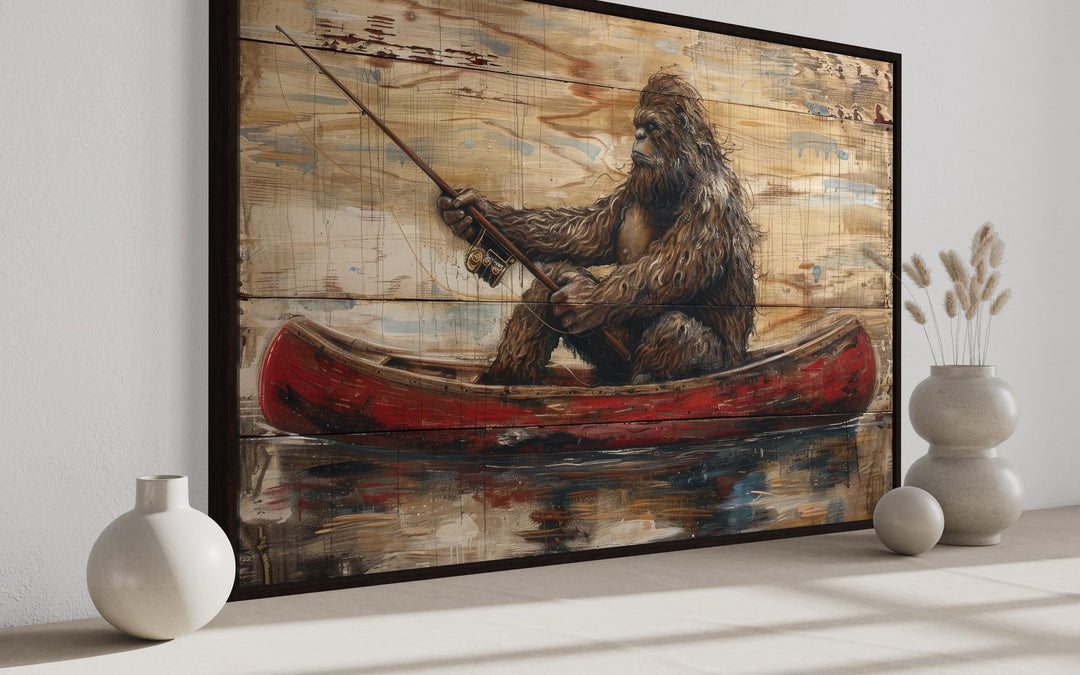Rustic framed canvas wall art of Bigfoot fishing in a red canoe on a wood-textured background.