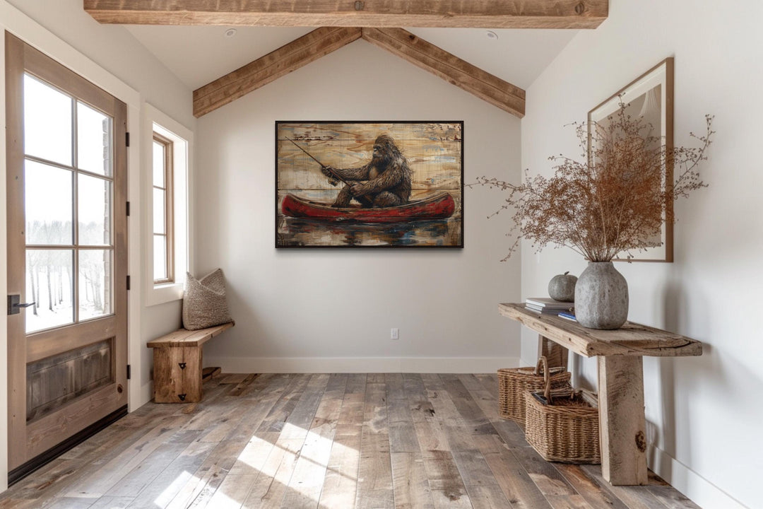 Bigfoot in a red canoe fishing, rustic framed canvas wall art in a cabin-style entryway.