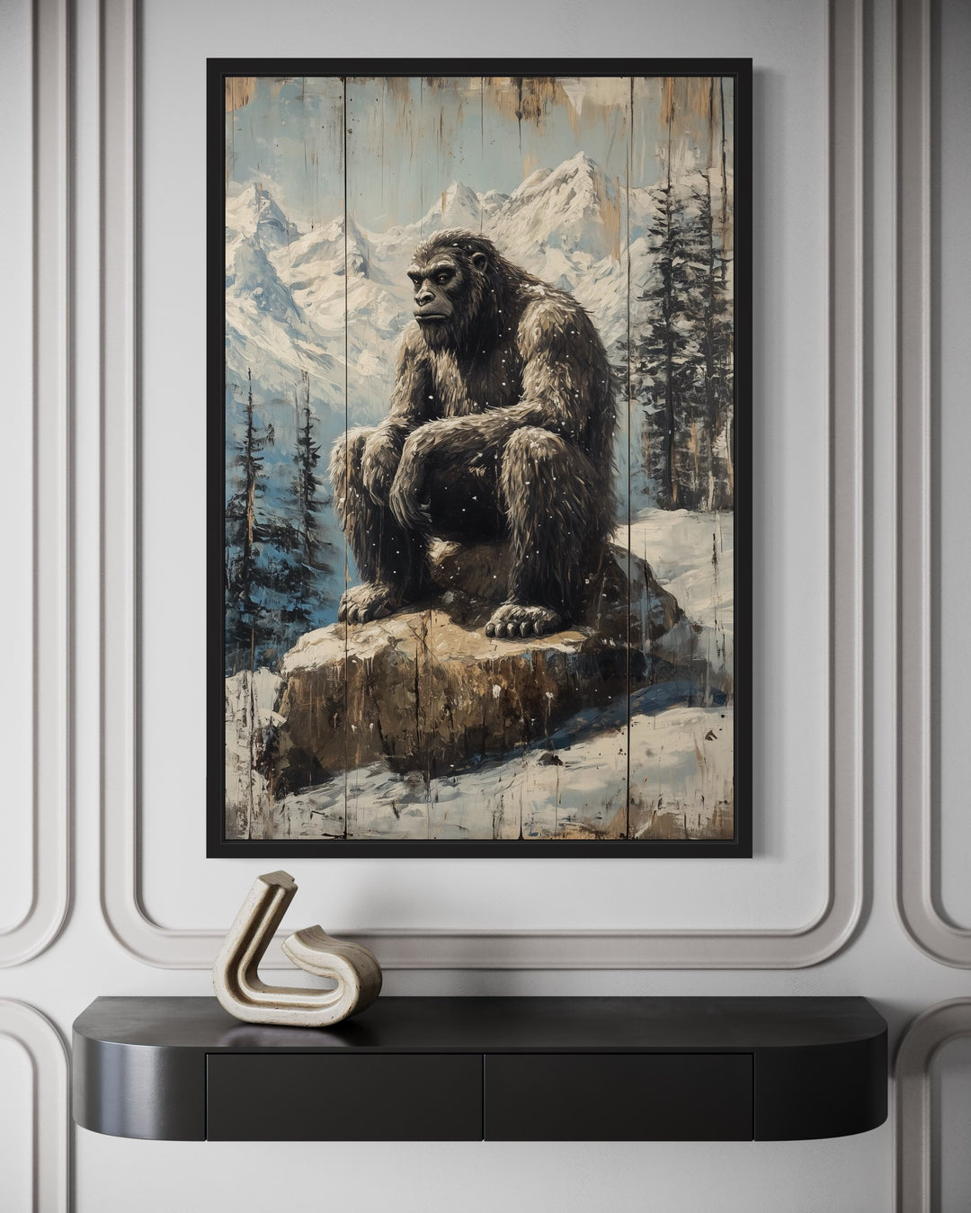 Bigfoot in snowy mountains painting on wood-effect framed canvas above a black console table.