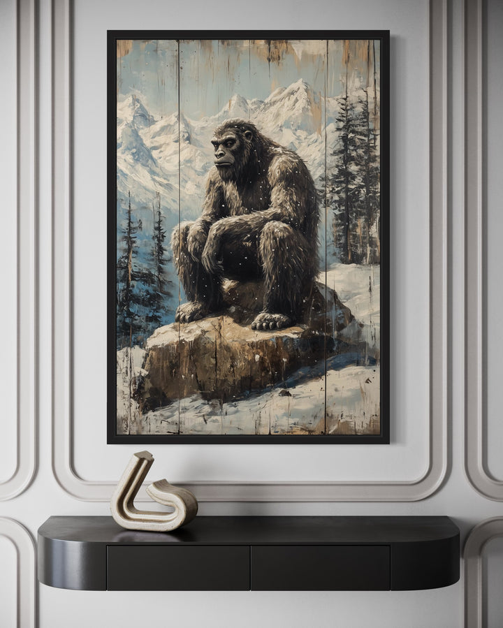 Bigfoot in snowy mountains painting on wood-effect framed canvas above a black console table.