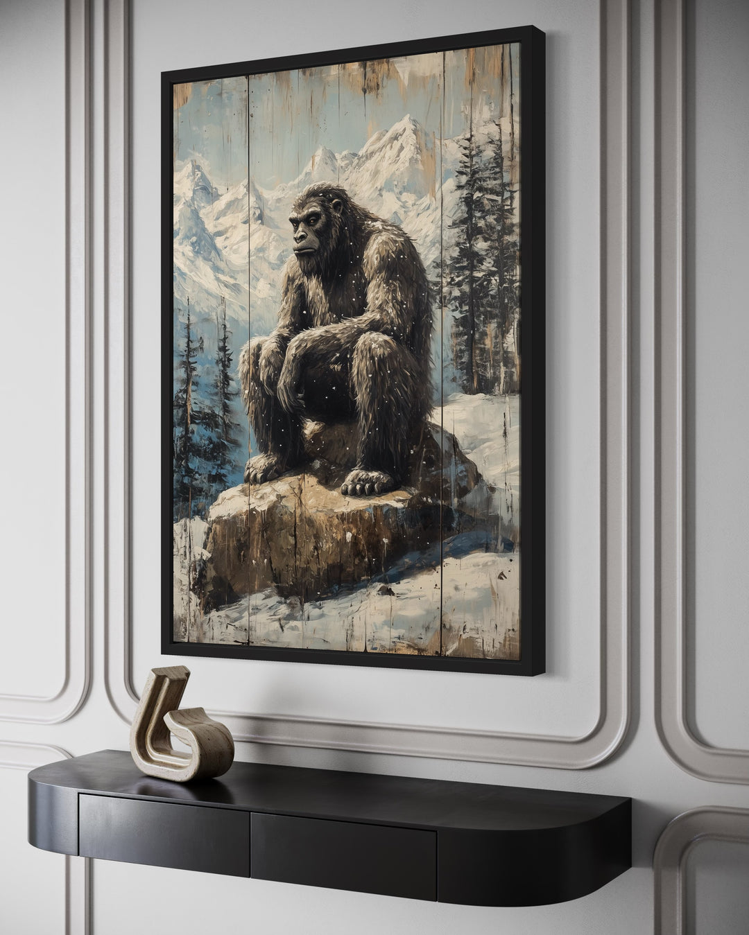 Framed canvas wall art of Bigfoot sitting on a rock in a snowy mountain landscape with pine trees.