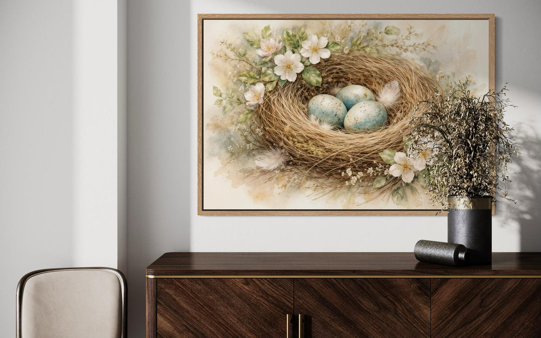 Bird nest wall art canvas print with blue eggs and pastel flowers above a dark wood sideboard.
